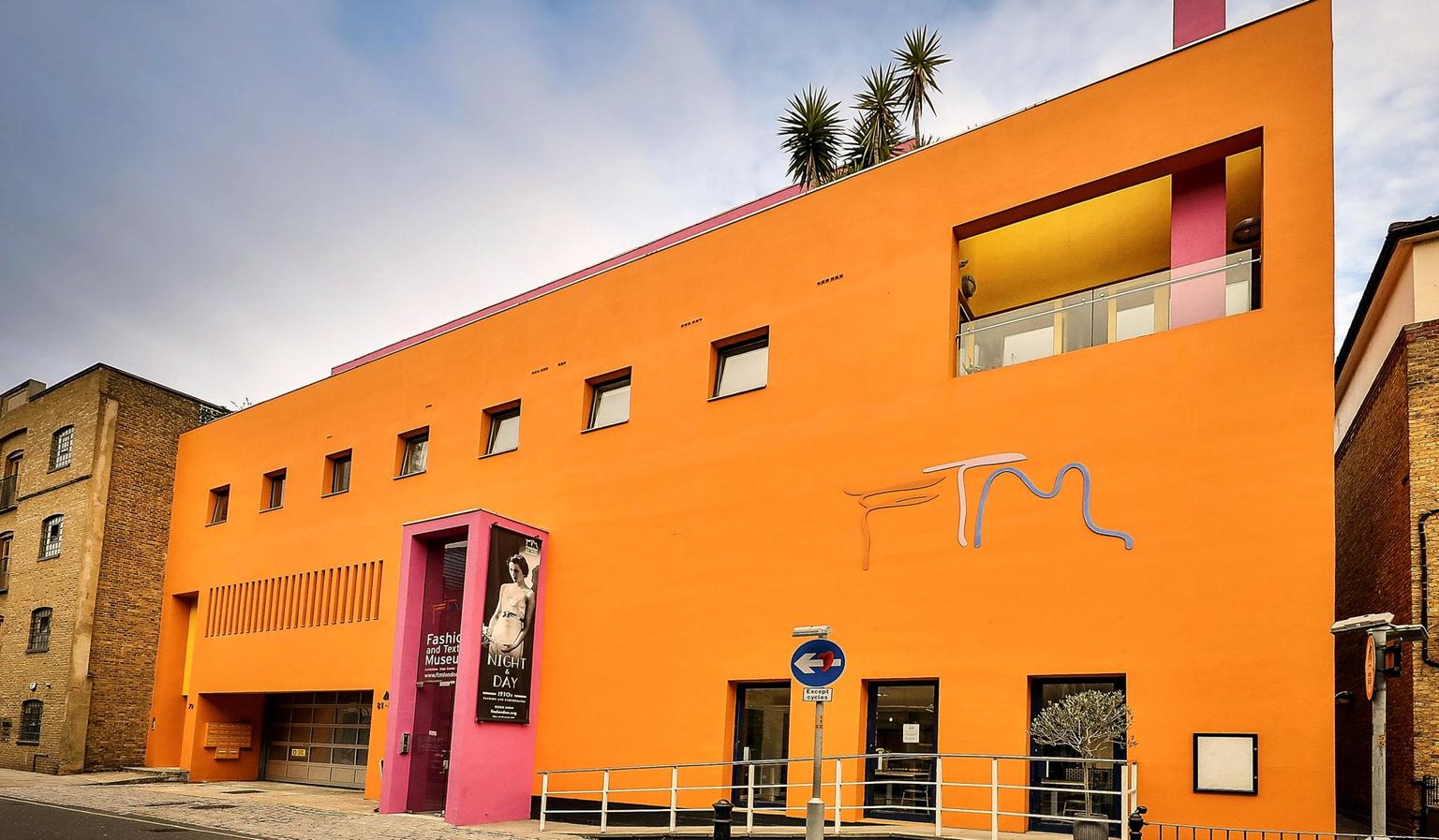 The exterior of a bright orange, rectangular building with a bright pink entryway