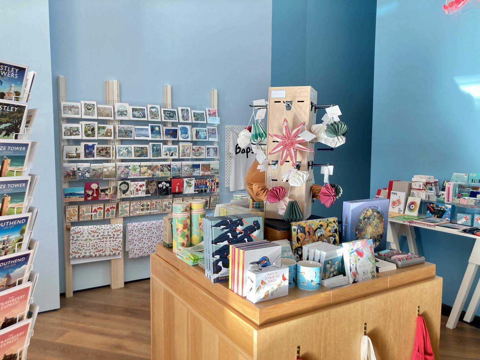 Inside Firstsite gift shop which has blue walls, postcard displays, Christmas gift wrap, an assortment of paper Christmas decorations, and lots of bird-related gifts, from mugs to books.