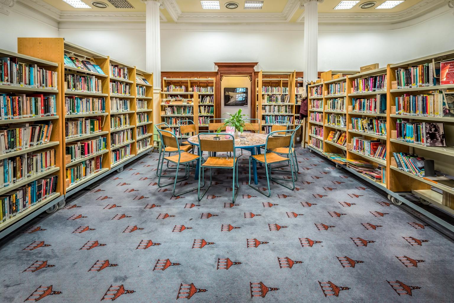 A brighly-lit library space with bookshelves and a circular table and chairs in the middle.