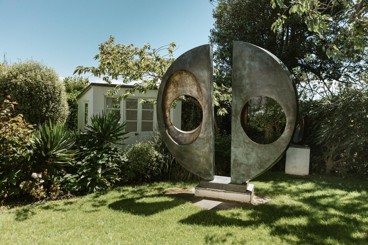 A metal sculpture formed of two halves of a circle, each with a hole in, set on a lawn in a garden