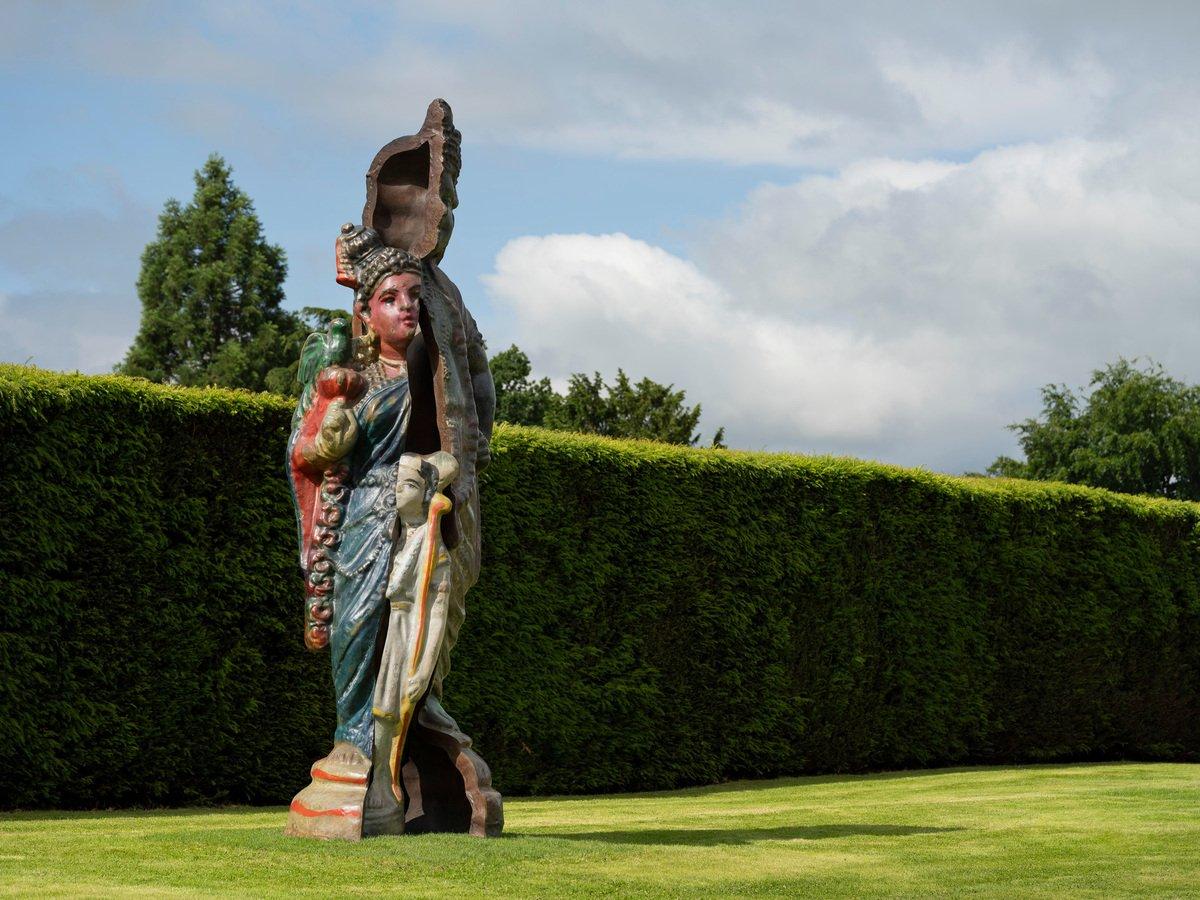 A sculpture made up of parts of a mother, father and son, set on a lawn with a high hedge behind it