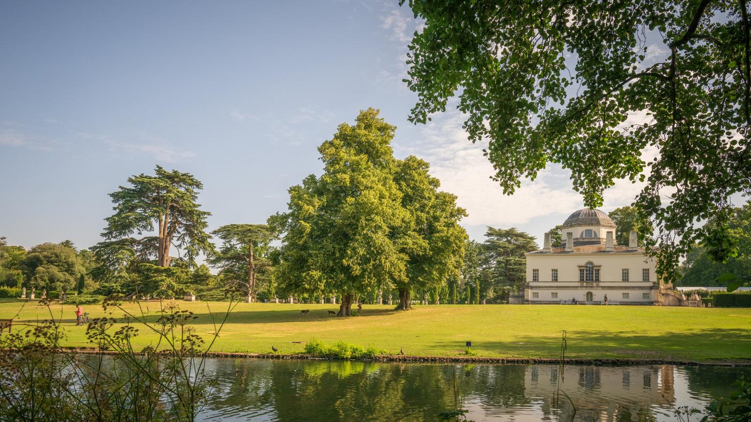 A riverside view overlooking wooded fields beyond and a manor house