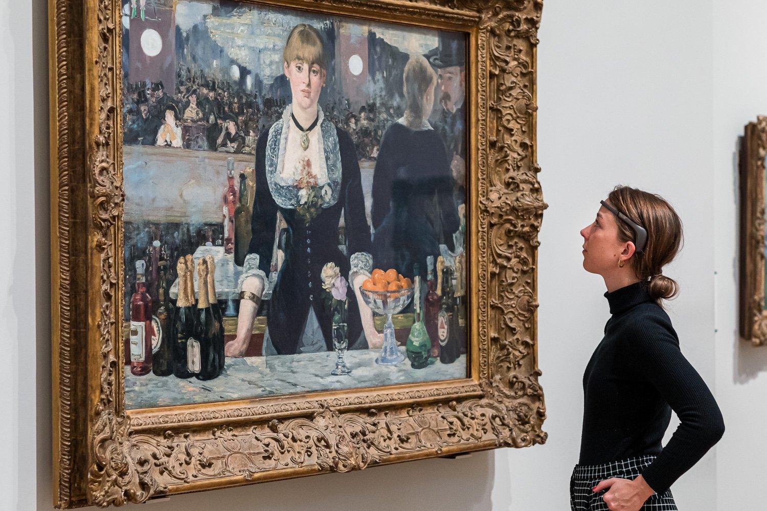 Visitor wearing a headset looks at a manet's Bar at the Folies-Bergere painting