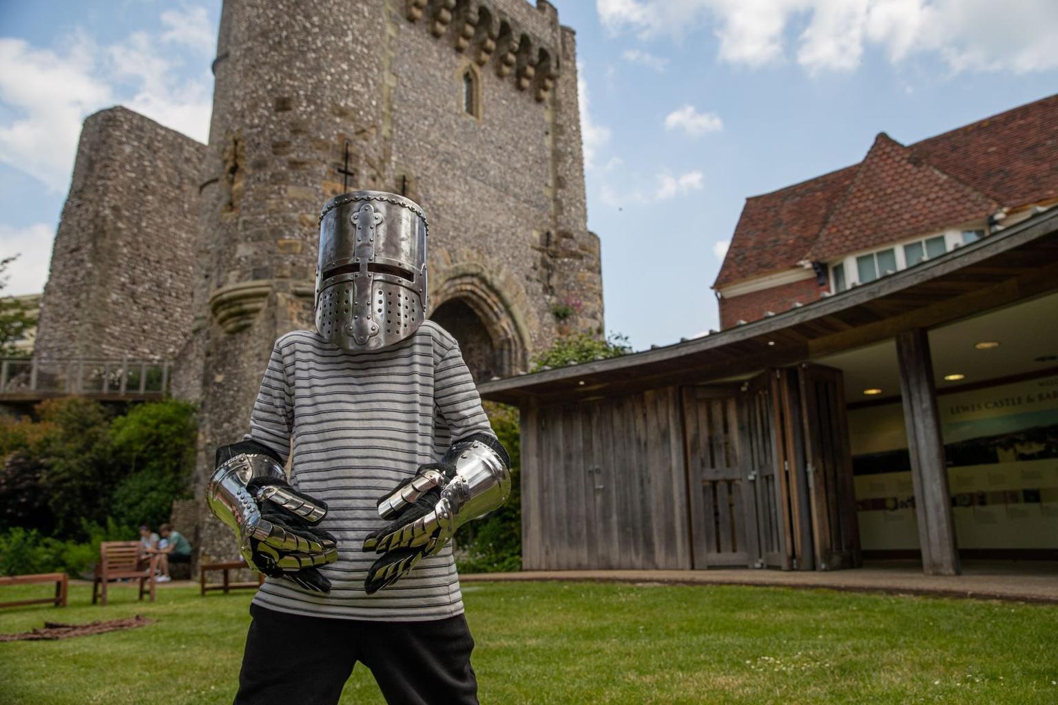 A child wearing a metal helmet and gloves with a castle keep in the background