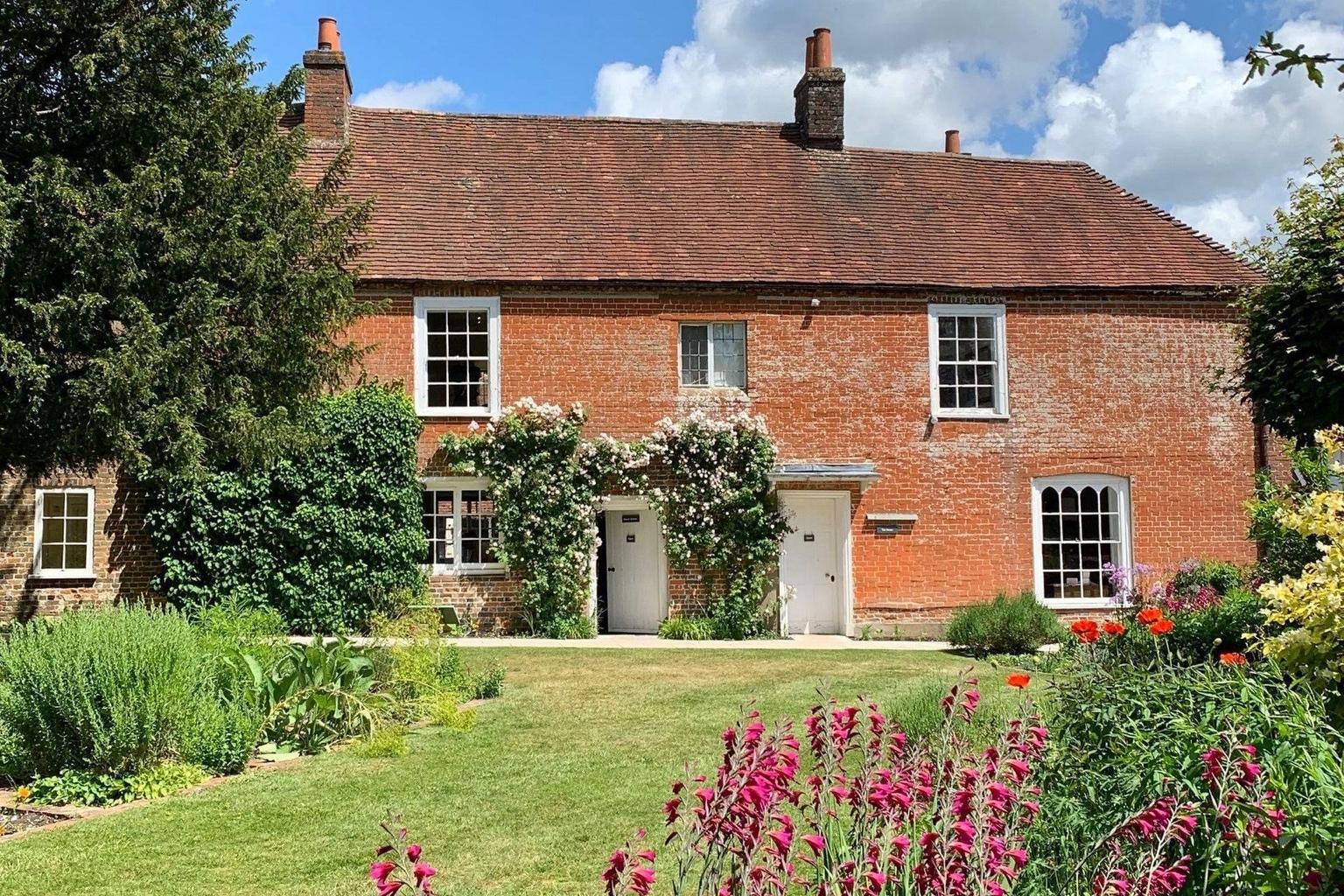 A brick house standing in a cottage garden, with pink flowers in the foreground