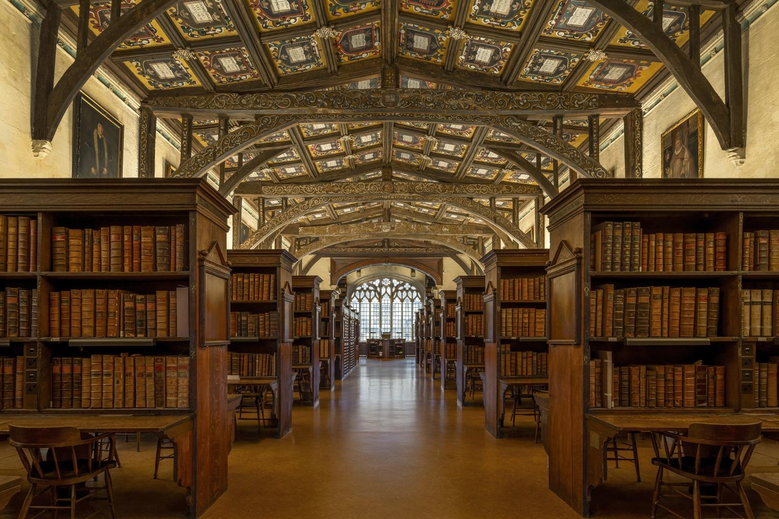 A historic library with rows of wooden bookshelves and an ornate patterned ceiling