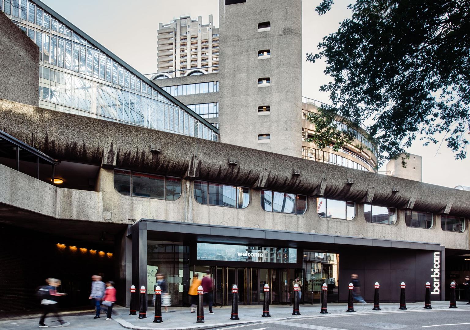 An entrance to a Brutalist building, with tower blocks behind