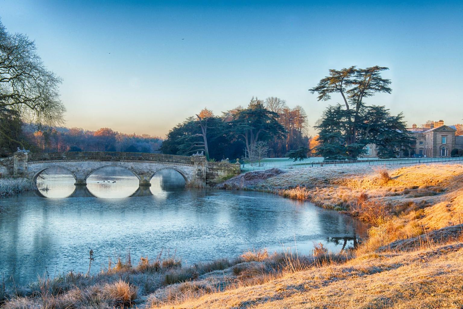 A frosty bridge, grounds and woodland lit by winter sunshine
