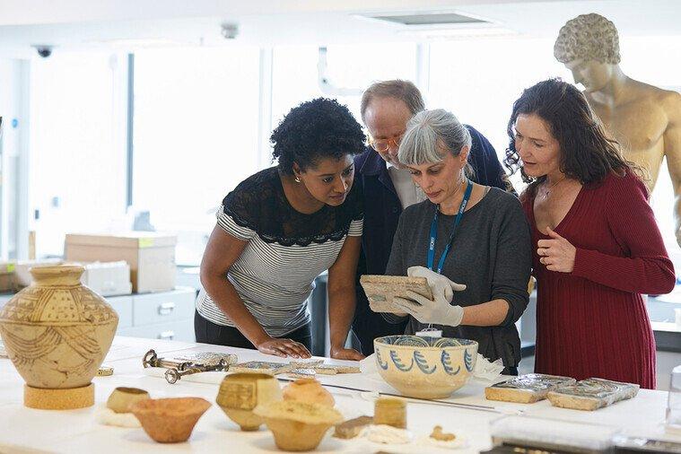 A group of people examine an tile held by a curator wearing white gloves