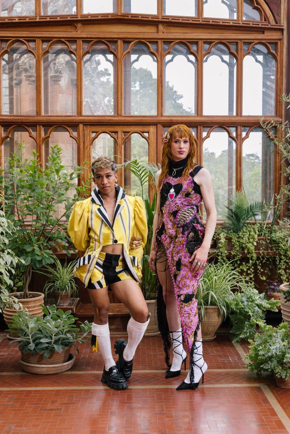 The artists Davide Bugarin and Angel Cohn Castle stand among potted plants in a bright wooden greenhouse.