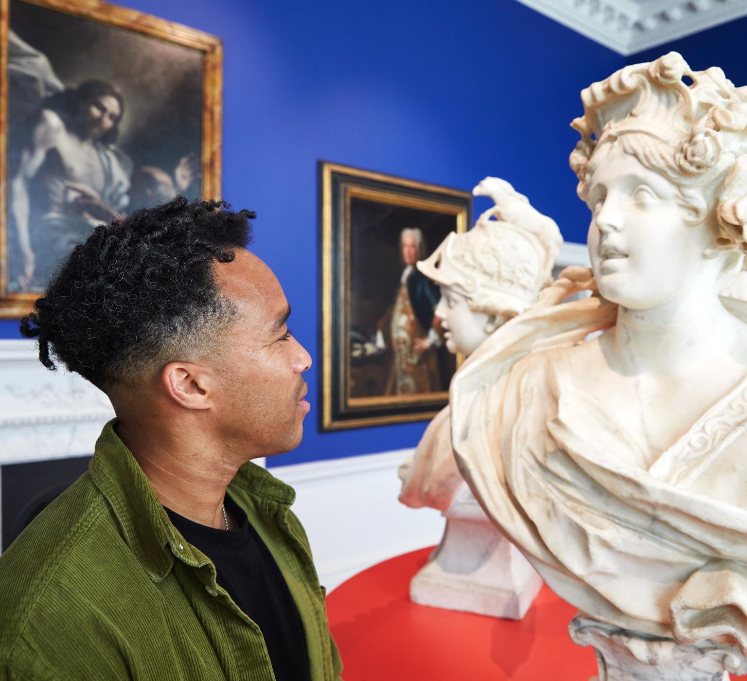 A man looking at a carved marble bust of a woman on a red pedestal