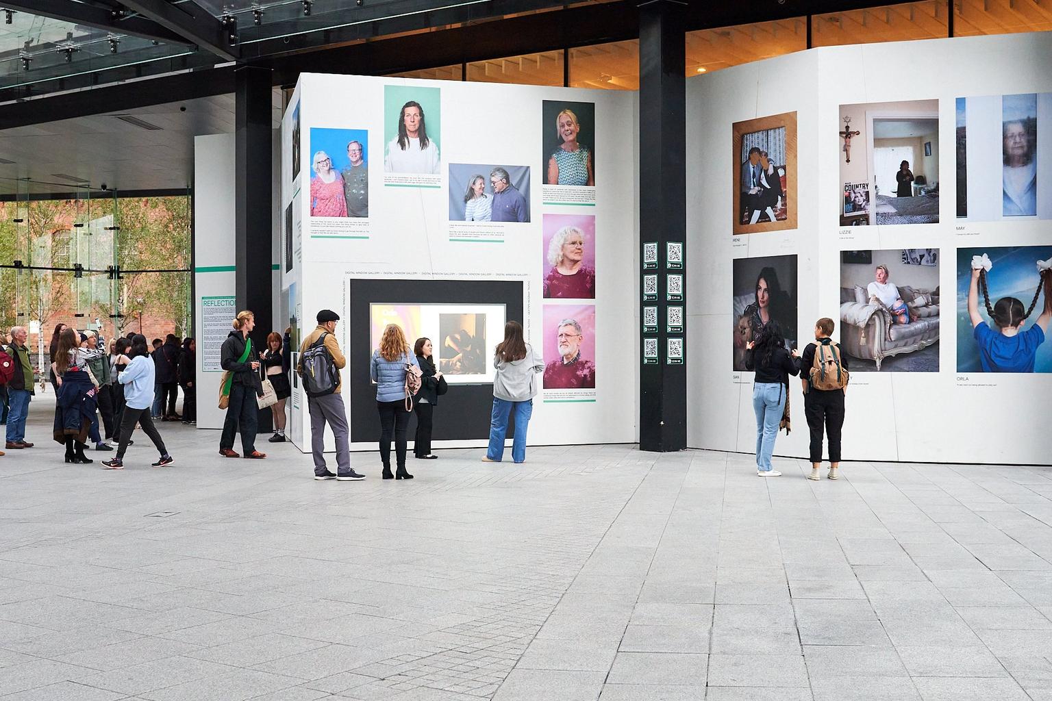 People looking at very tall white walls covered in large prints of photographs
