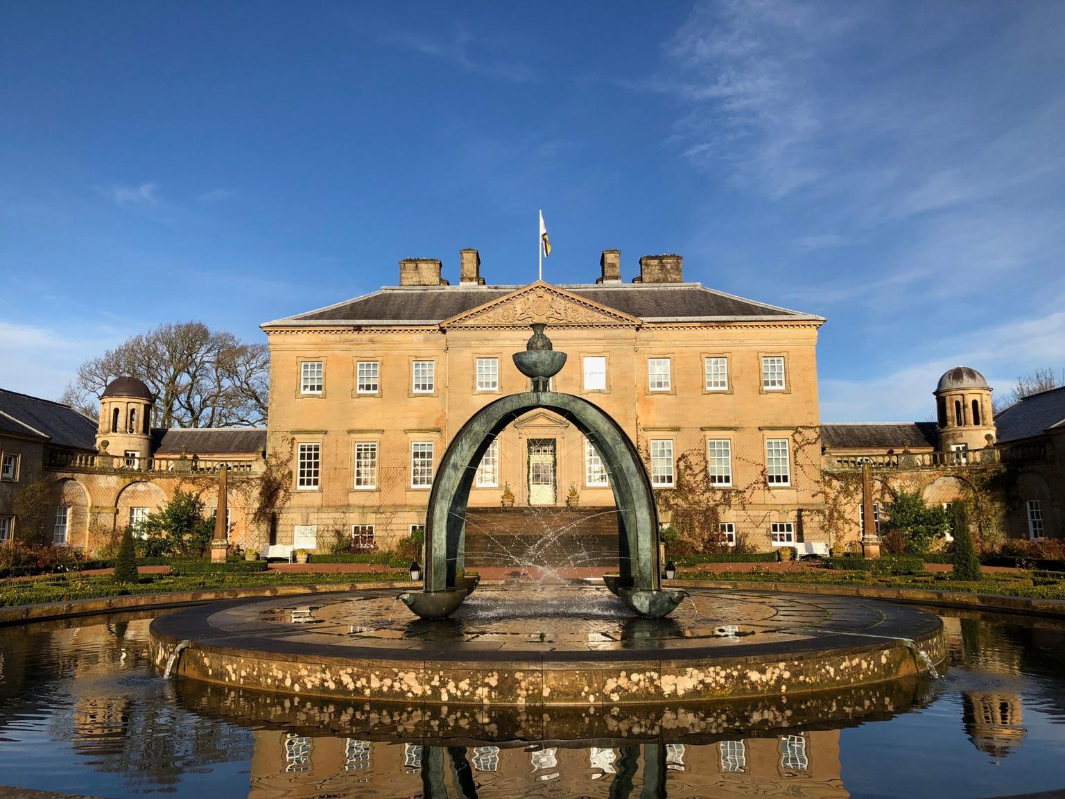 A fountain in front of a manor house, blue skies above