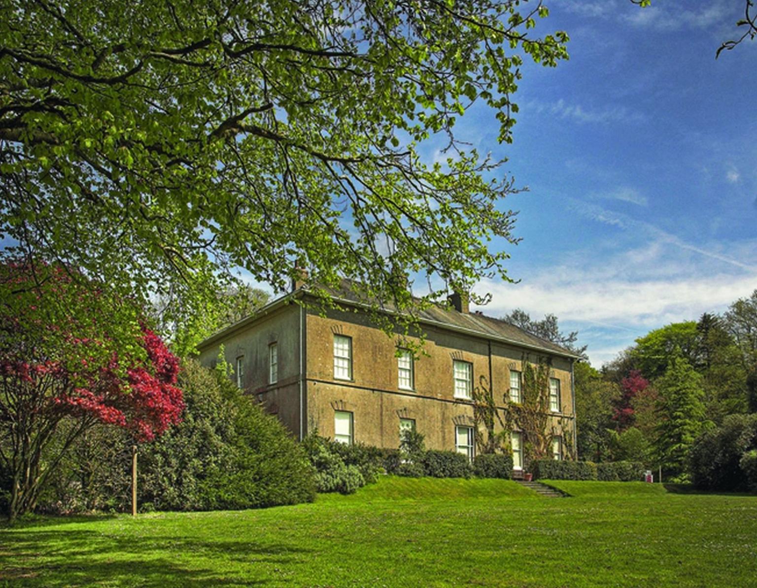 A historic house fronted by lawns and trees, blue skies behind
