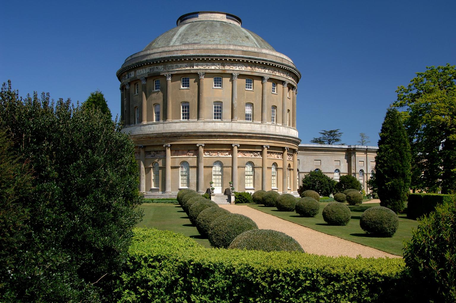 A rotunda building with domed roof and columns, fronted by spherical box hedges alongside a path