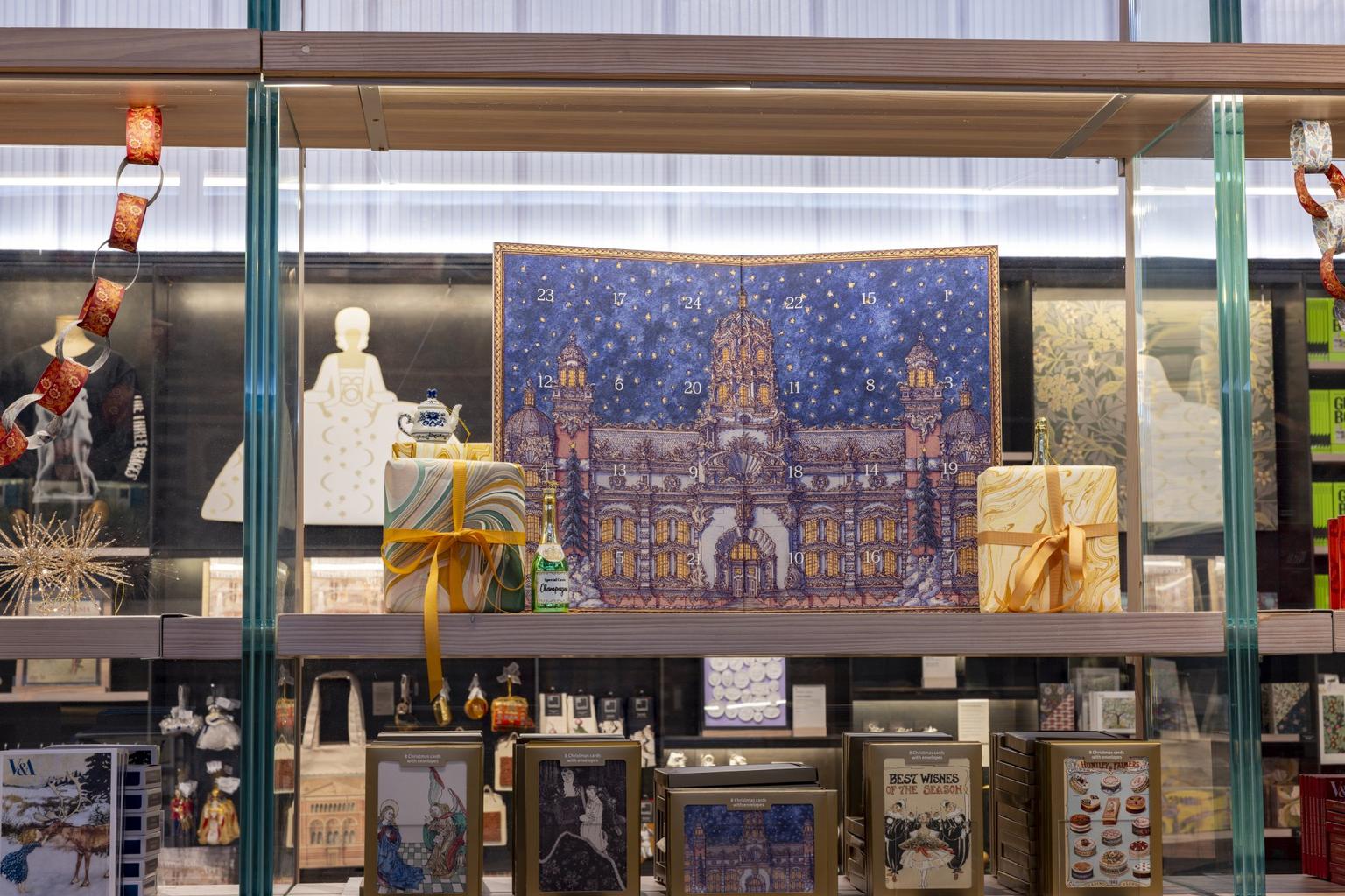 A gift shop display features Christmas cards, wrapped gifts, and a blue starry advent calendar depicting a lit historic building flanked by wrapped gifts and festive items.