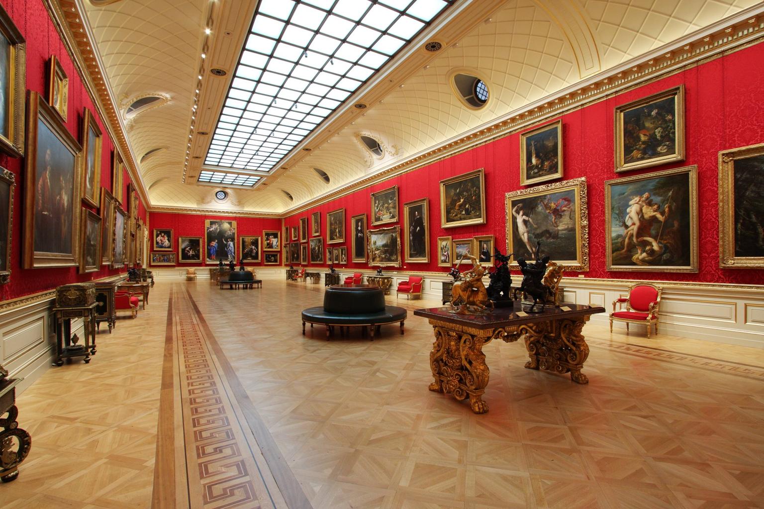 A long art gallery with red brocade walls and a parquet floor