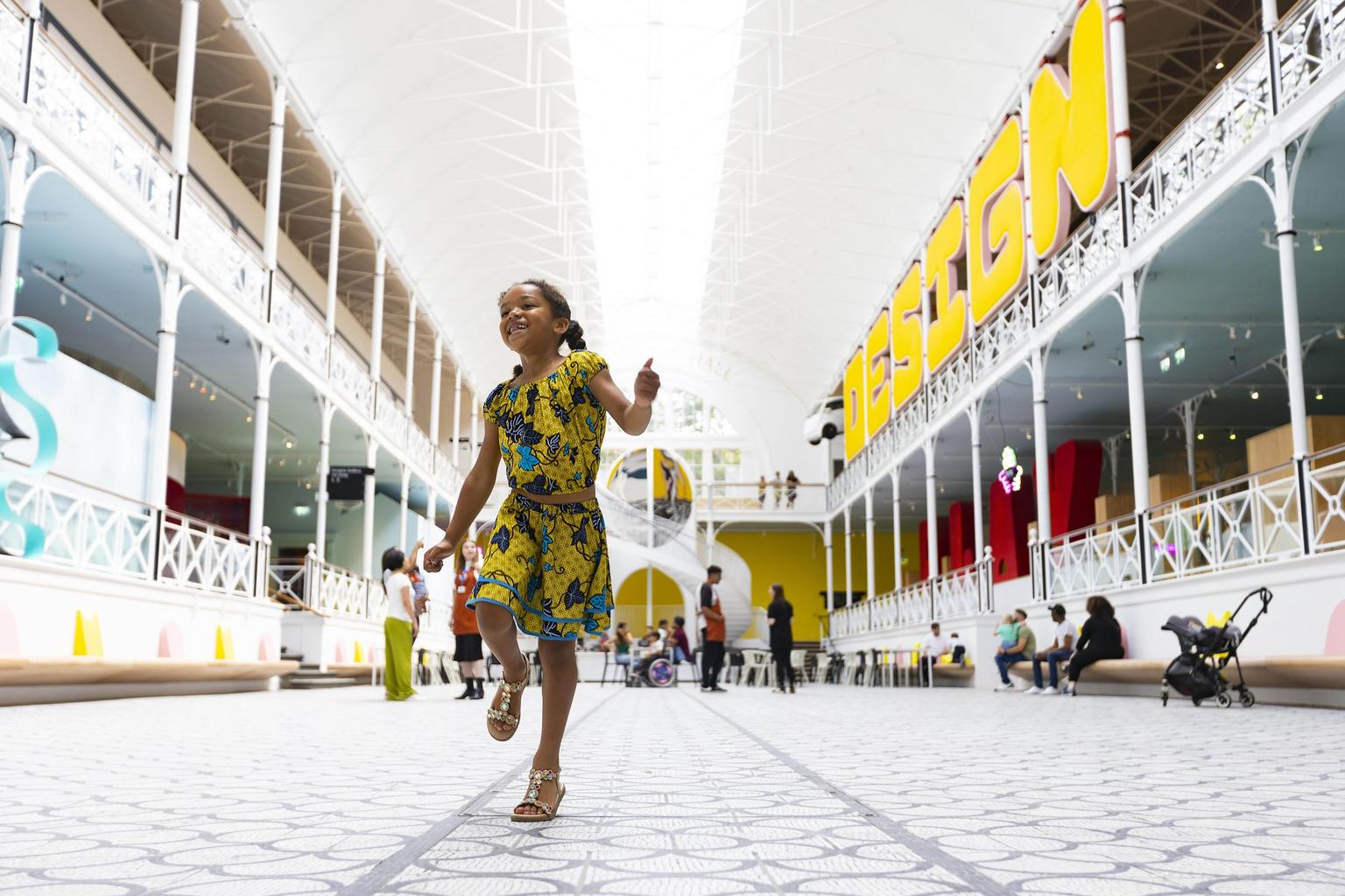 Girl in a yellow dress walks through the main space in the Young V&A