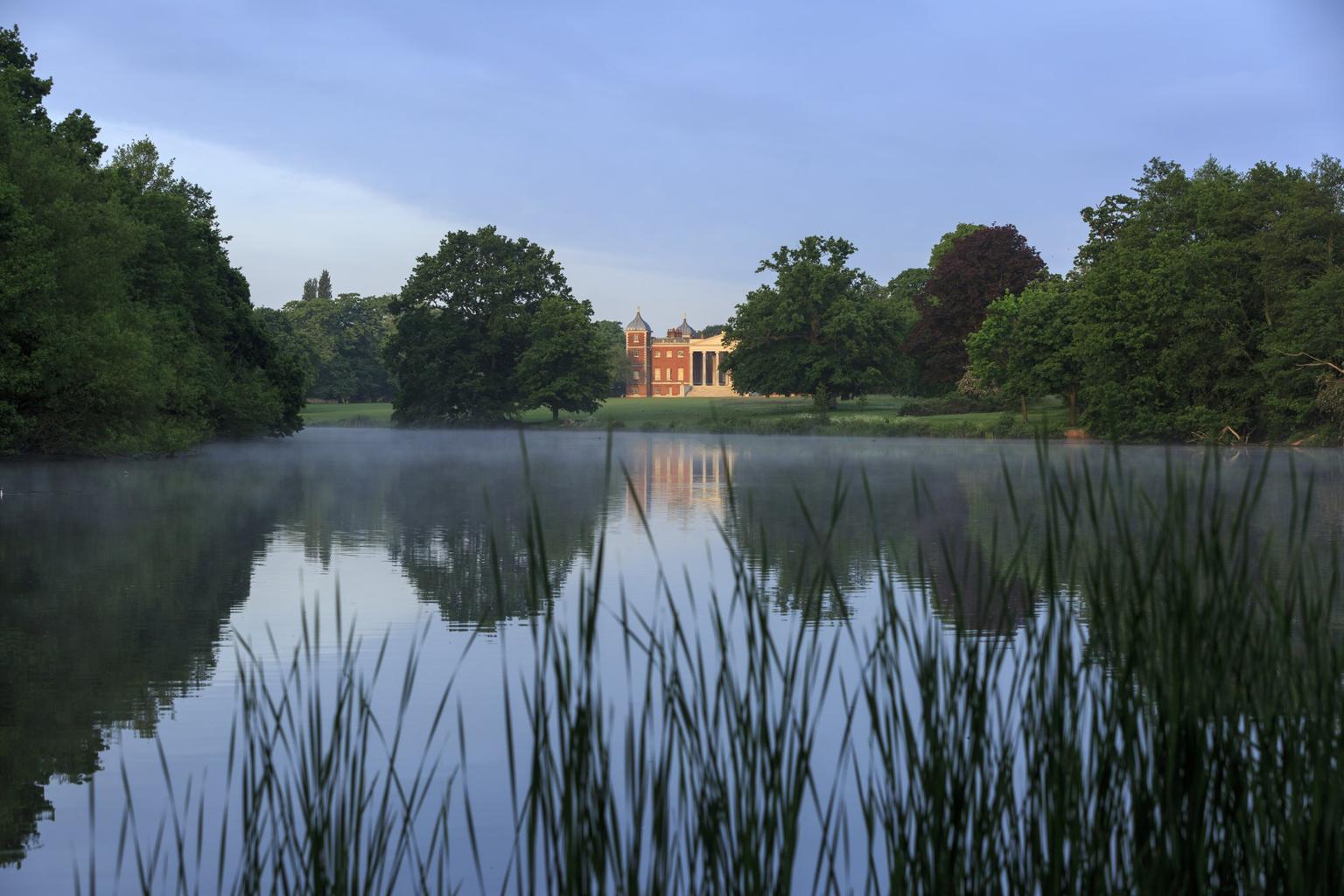 A large lake with a stately house and large trees on the far bank