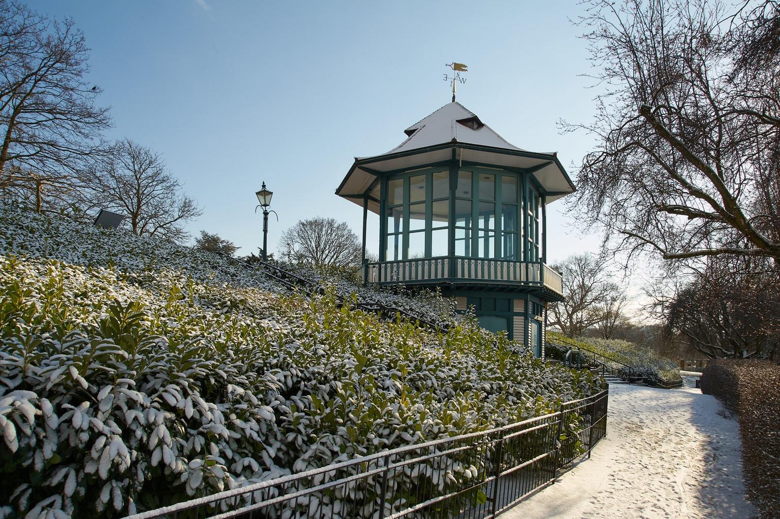 Snow dusting evergreen bushes and a path to a green painted bandstand
