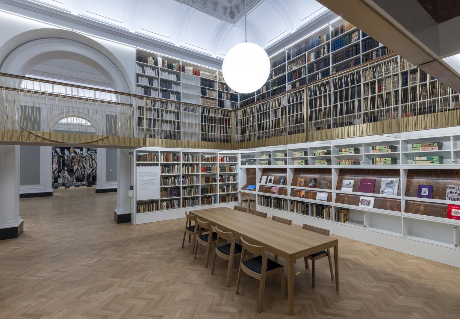 Ceiling-high bookshelves of photography books with a balcony, fronted by a wooden table and chairs on a parquet floor