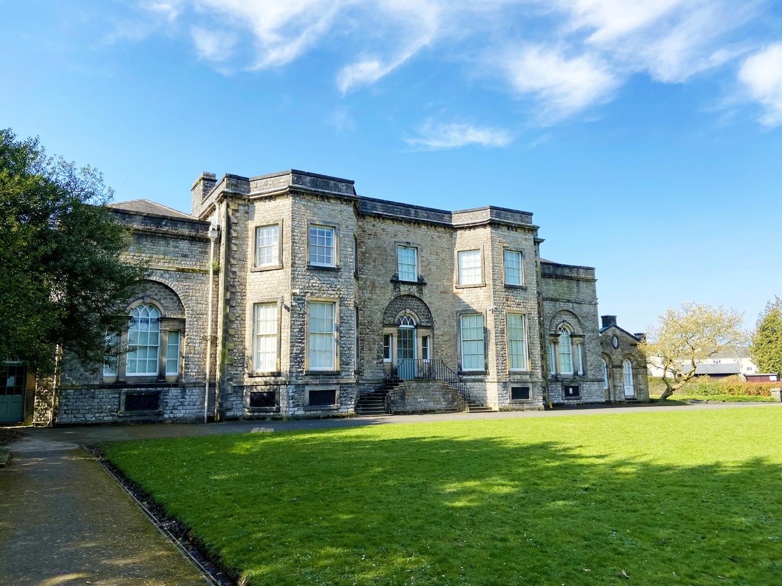 The front of a Georgian building on a sunny day, with a lawn in front and tree to the left