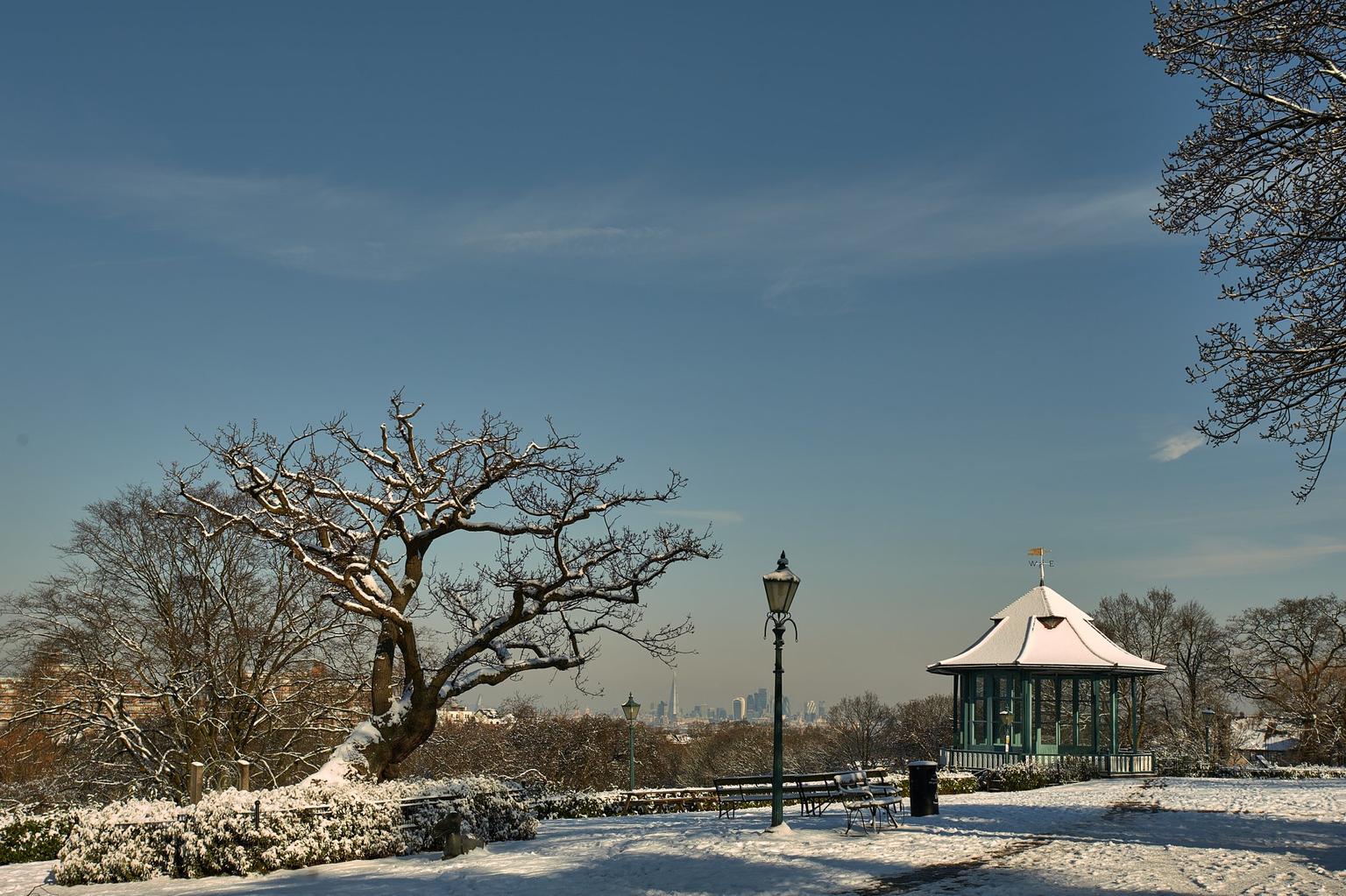 Gardens and trees covered in snow with a bandstand and iron lamppost