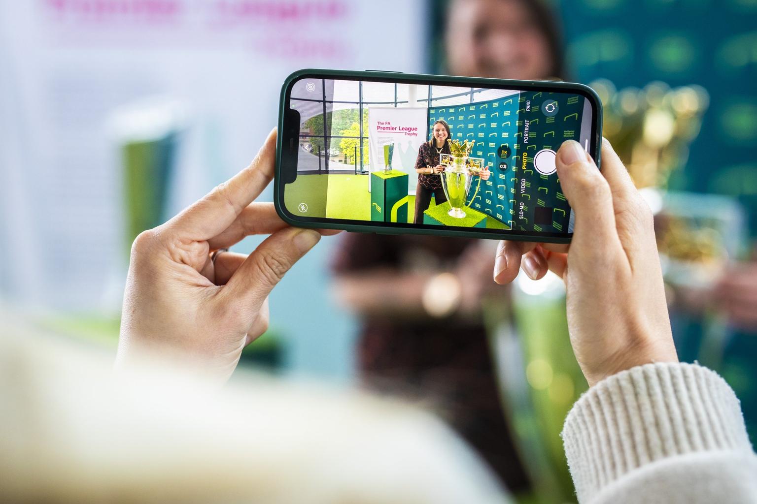 Hands holding up a cameraphone with a woman holding a trophy shown in the photo