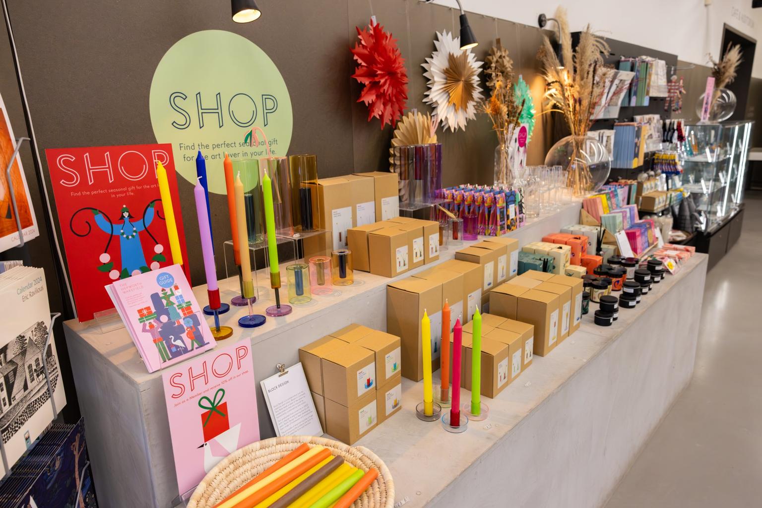 A colorful gift shop display with neon dinner candles, boxed homewares and festive paper star decorations.