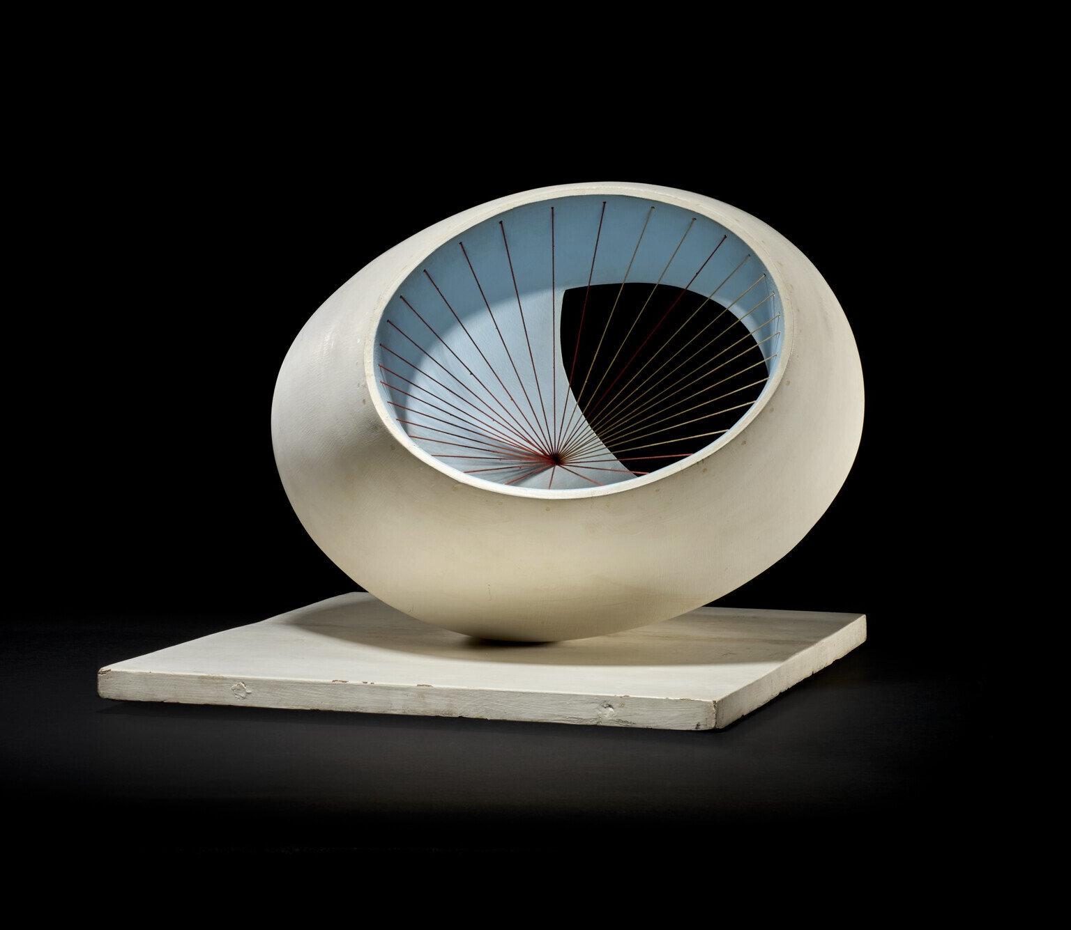 A smooth white oval sculpture with a sky-blue interior and radiating black strings anchored at a red center, displayed on a square white base against a black background.