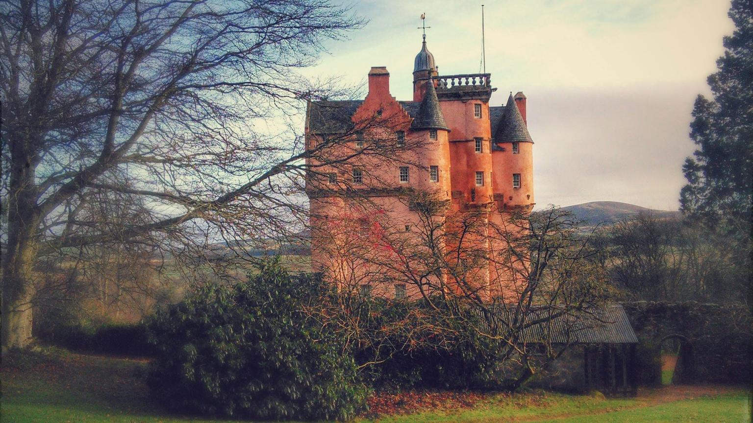 A hazy photo of the pink walls of Craigievar Castle, behind a wall and trees
