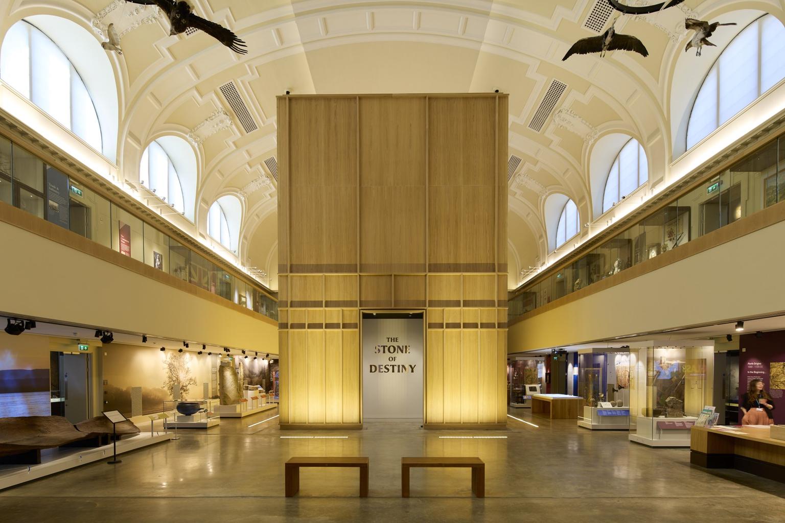 The interior of a light museum space with glass displays along the sides, and a large wooden structure with the sign 'The Stone of Destiny' on the entrance.