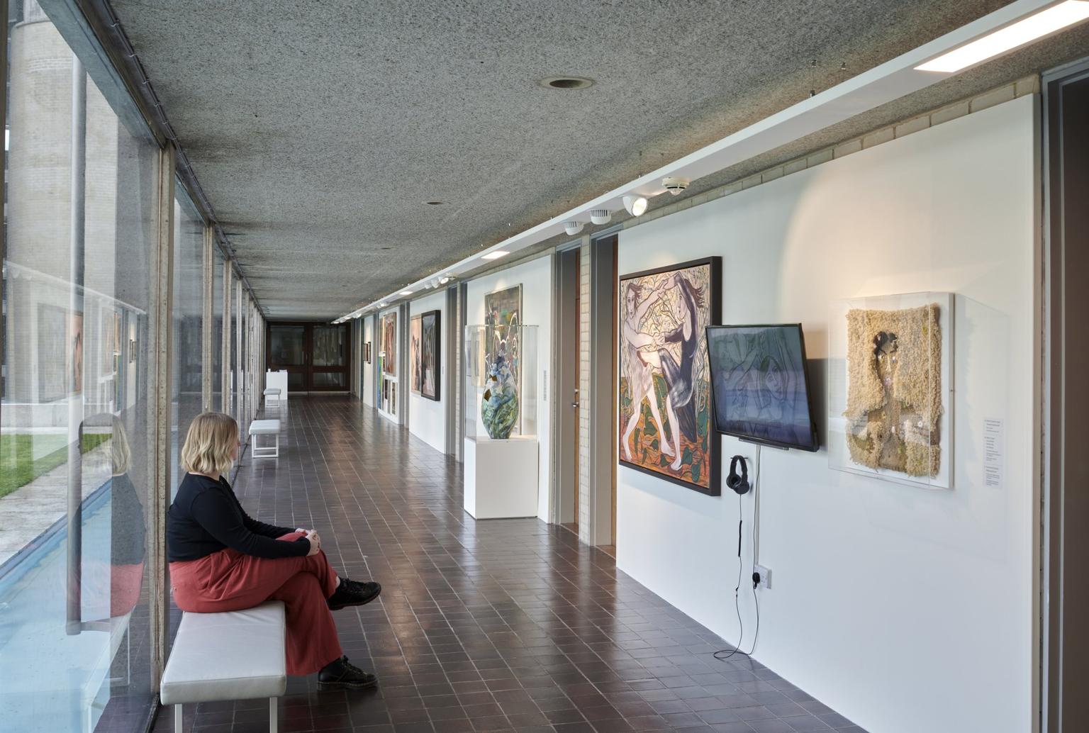 A hallway with one glass wall and a woman sitting to look at art on the other wall