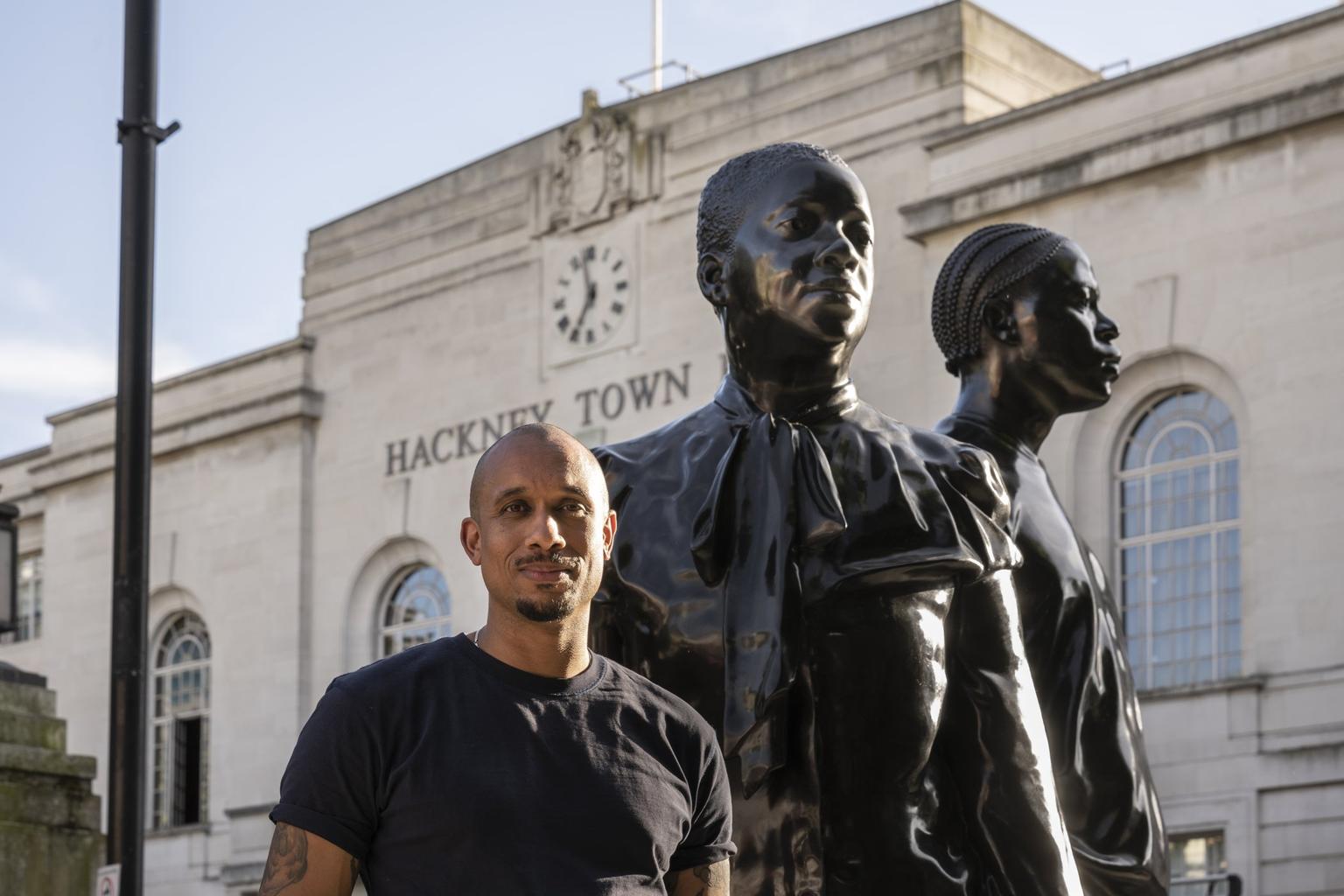 Thomas J Price standing in front of a sculpture of two people outside Hackney Town Hall