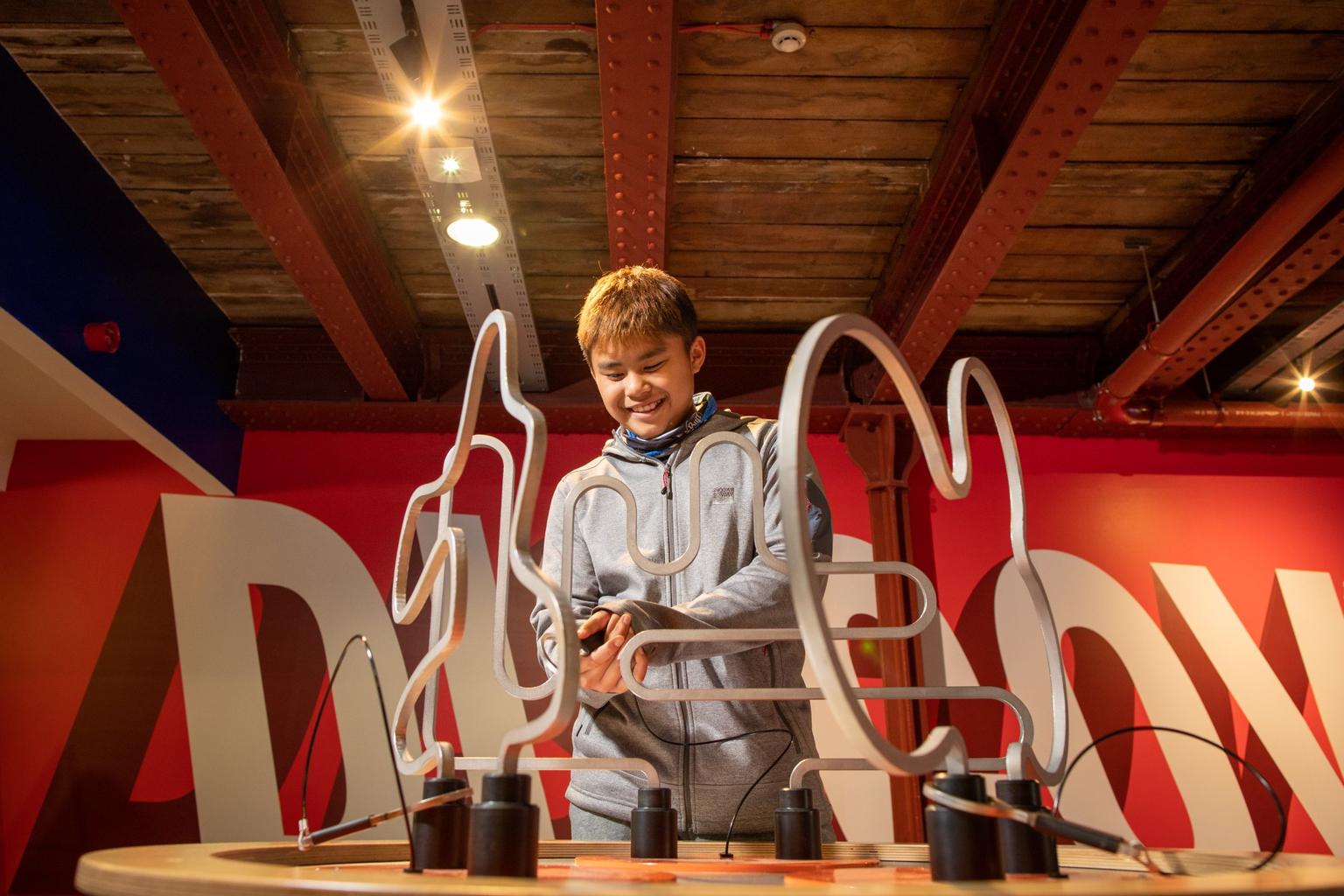 A boy tries to get a metal loop to the other side of a buzz wire game