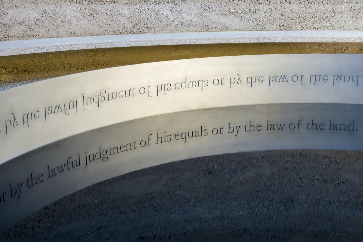 The side of a sculpture inscribed with upside down writing so that it can be read in the pool below