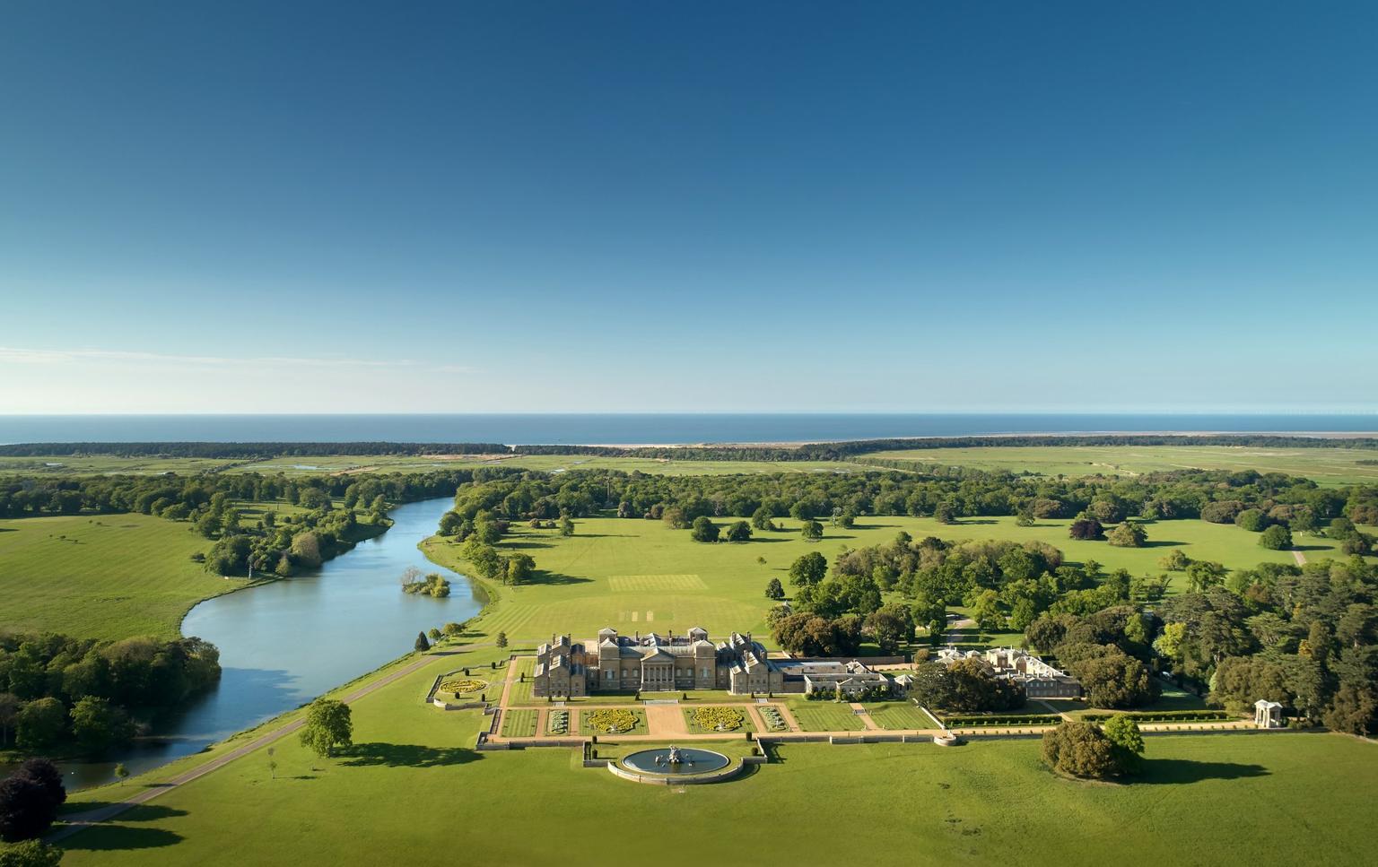 An arial view of a house and grounds, surrounding river and trees, with a beach in the distance