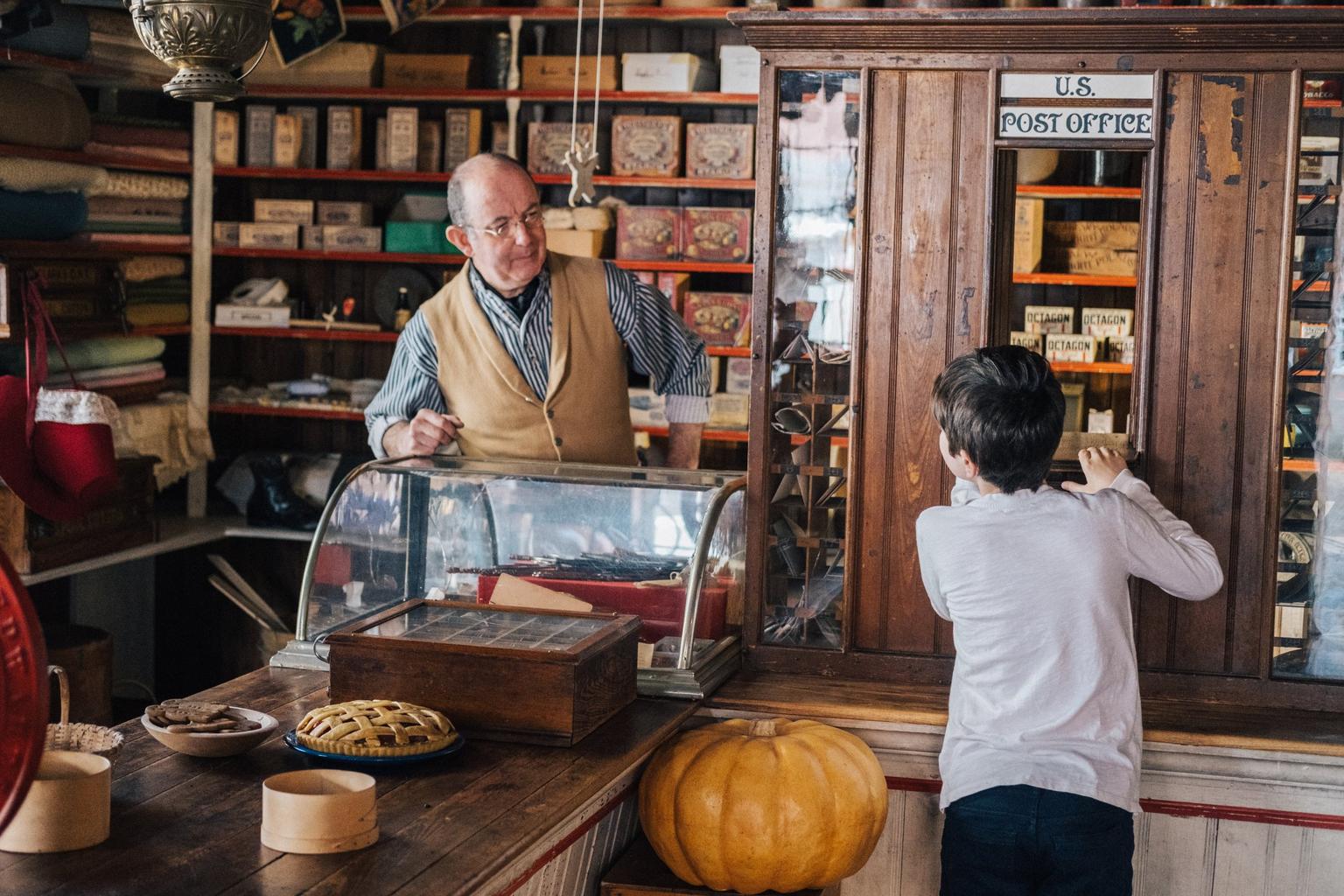 The interior of a heritage post office, with man behind the counter and boy looking at the shelves