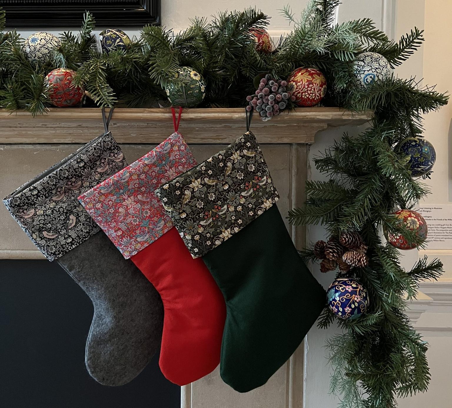 Three Christmas stockings hang from a fireplace decorated with a Christmas tree branch and Christmas baubles.