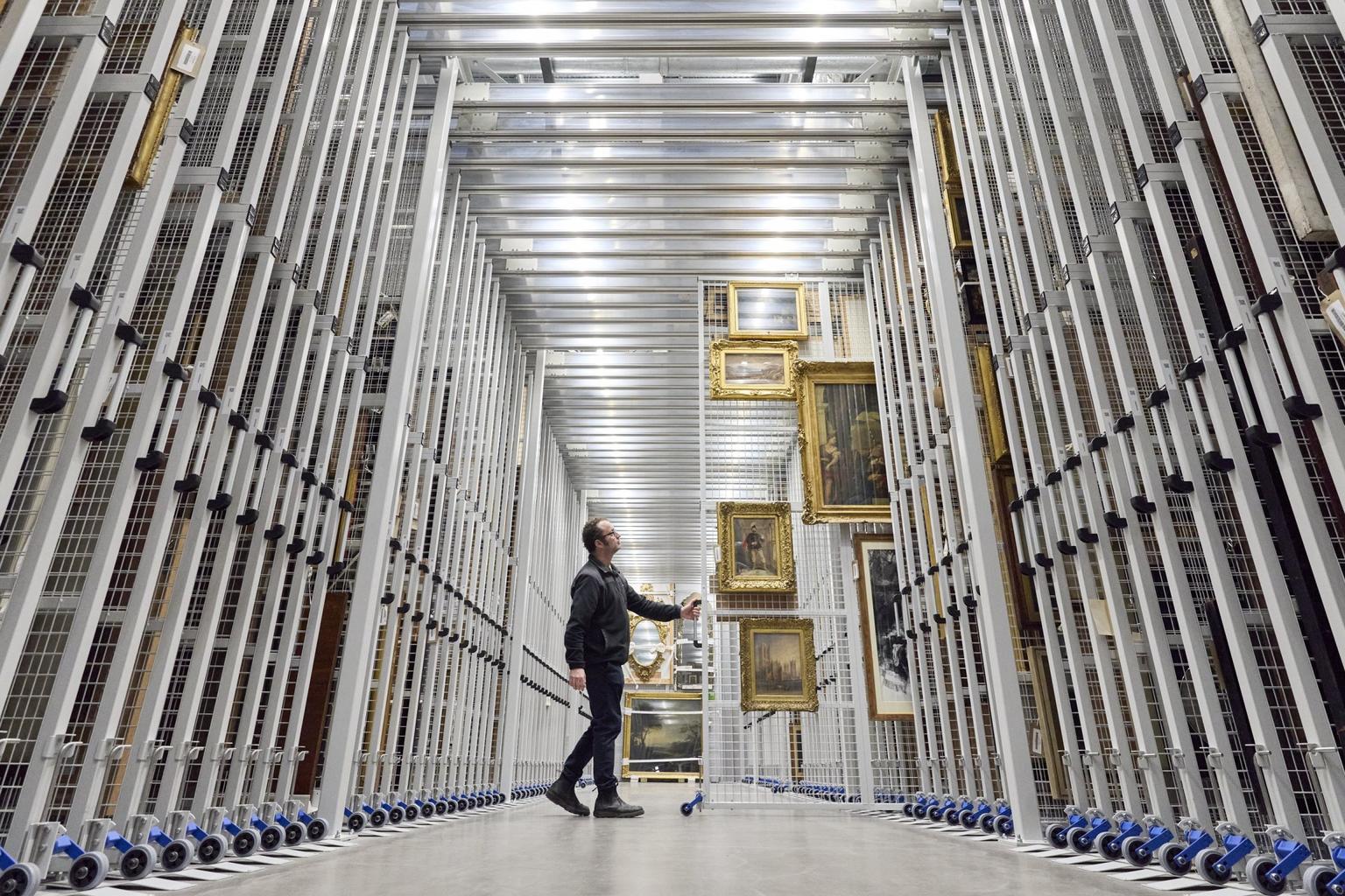 A man draws out a metal frame hung with paintings in a storehouse