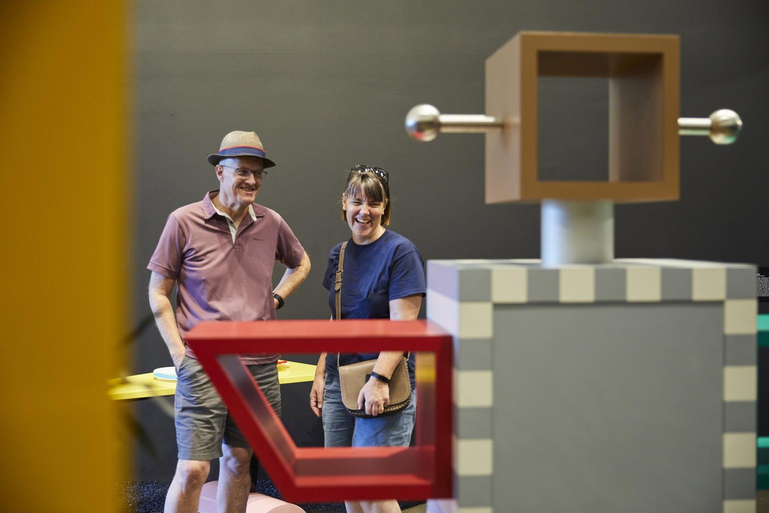Visitors smile looking at a robot-shaped sculpture