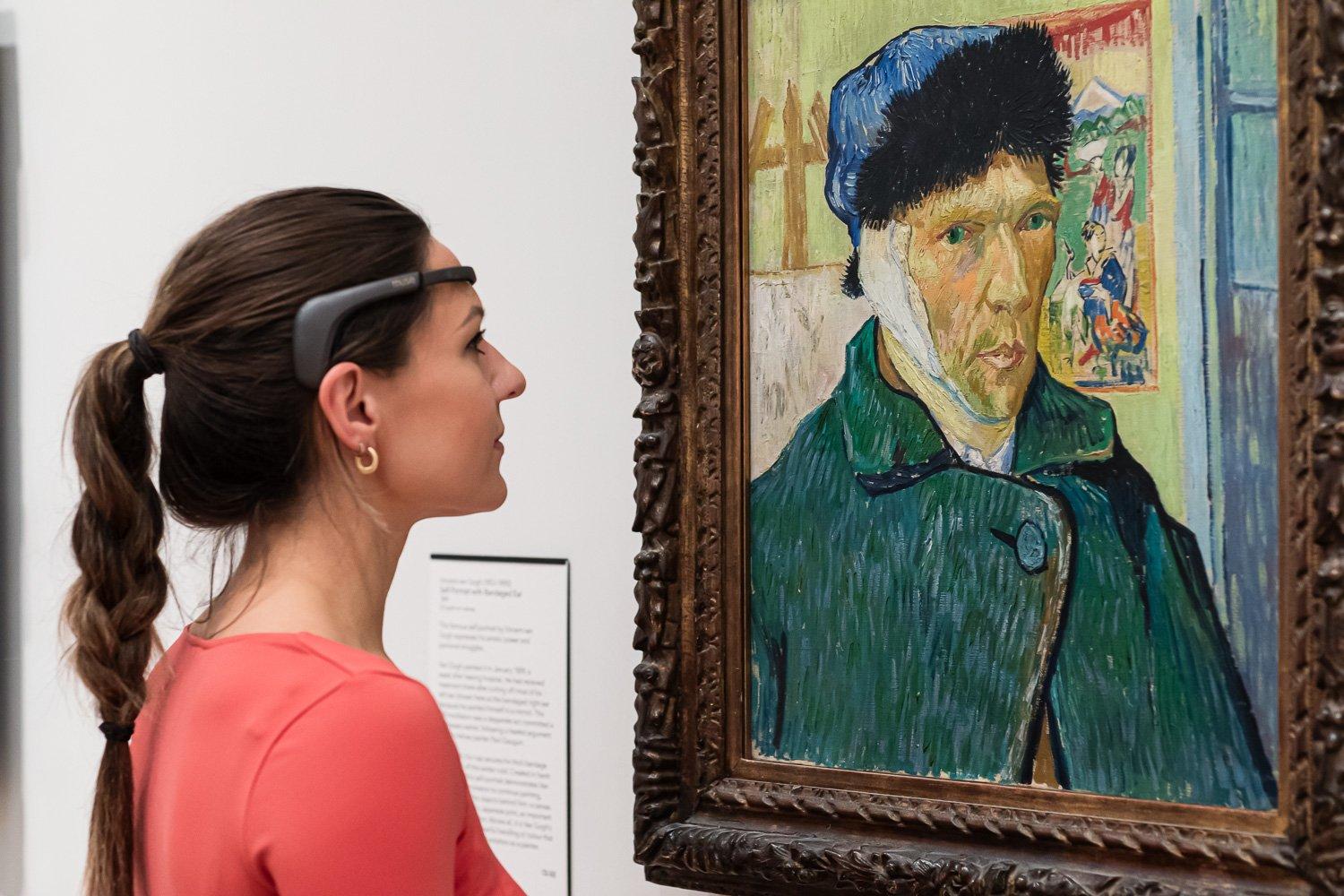 A visitor wearing a headset looks at a Van Gogh portrait