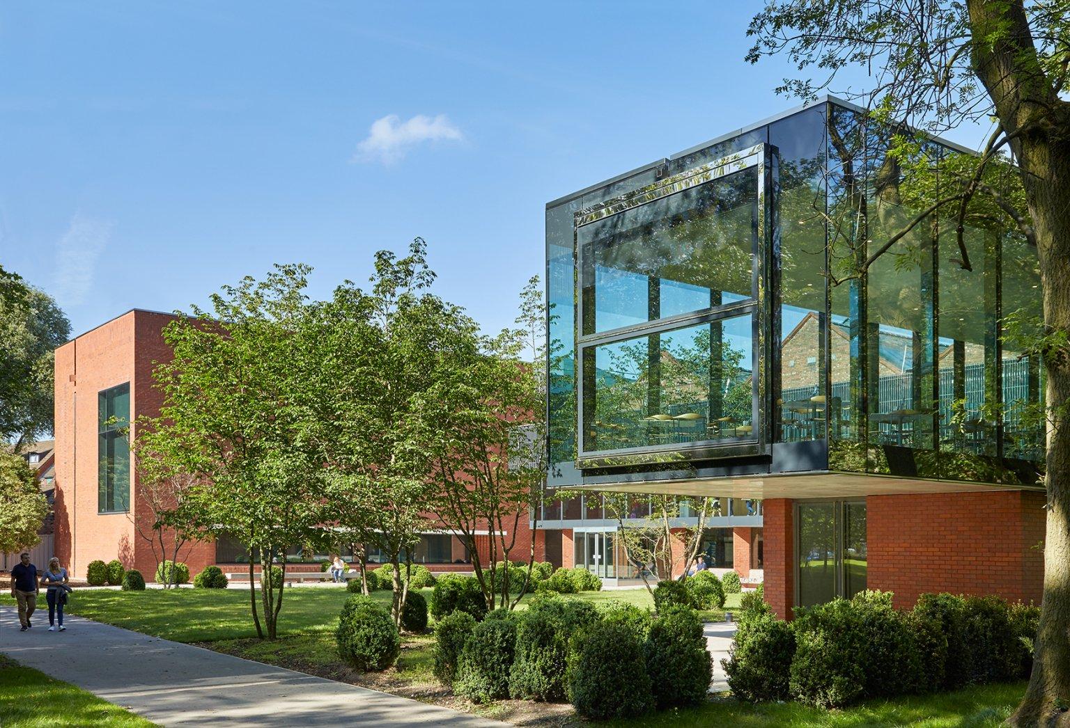 A glass and brick building surrounded by gardens and trees