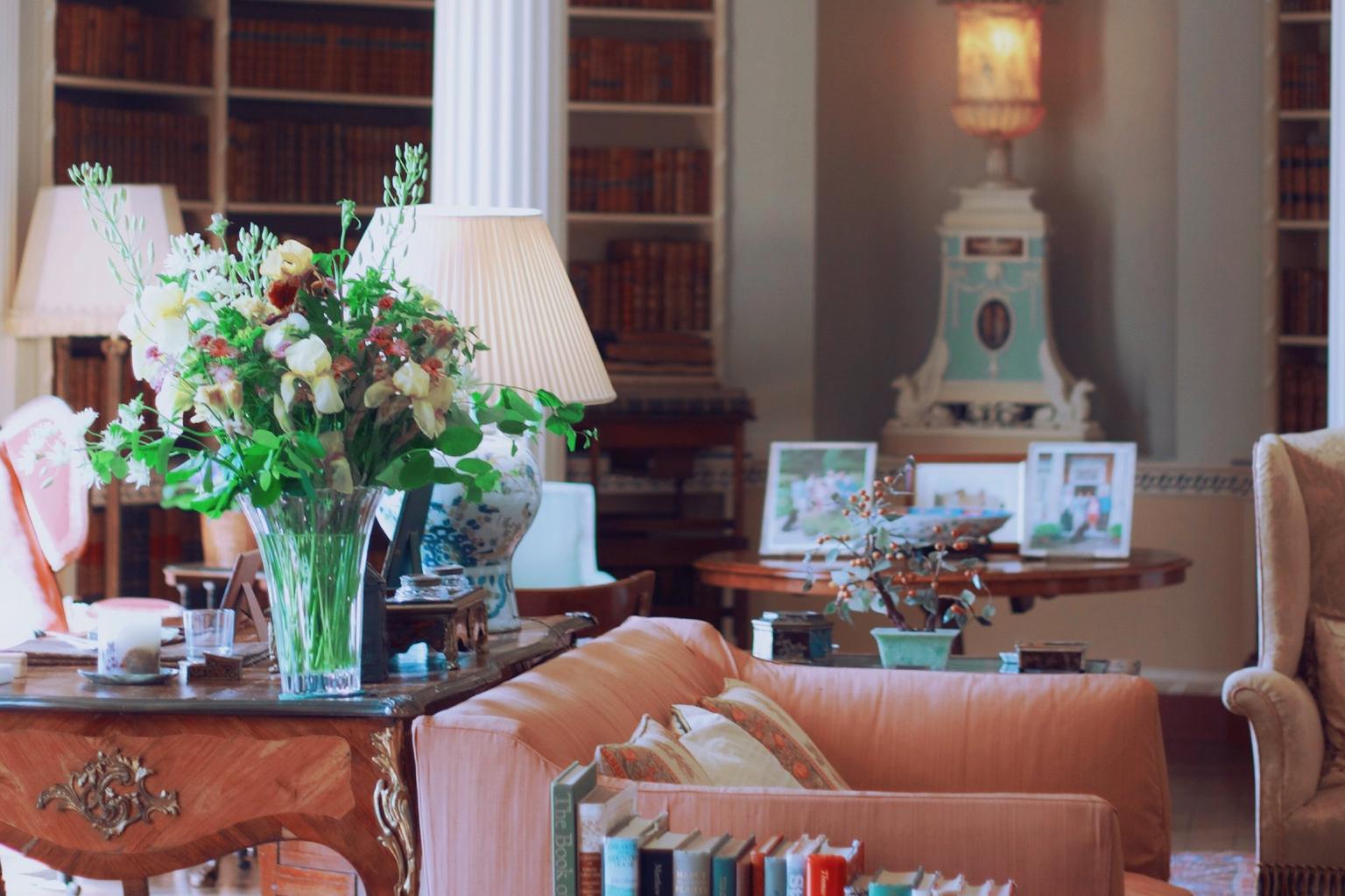 An ornate library with columns, antique furniture, flowers and a pink sofa