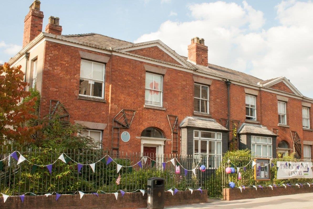 A red bricked house with railings and bunting in suffragette colours