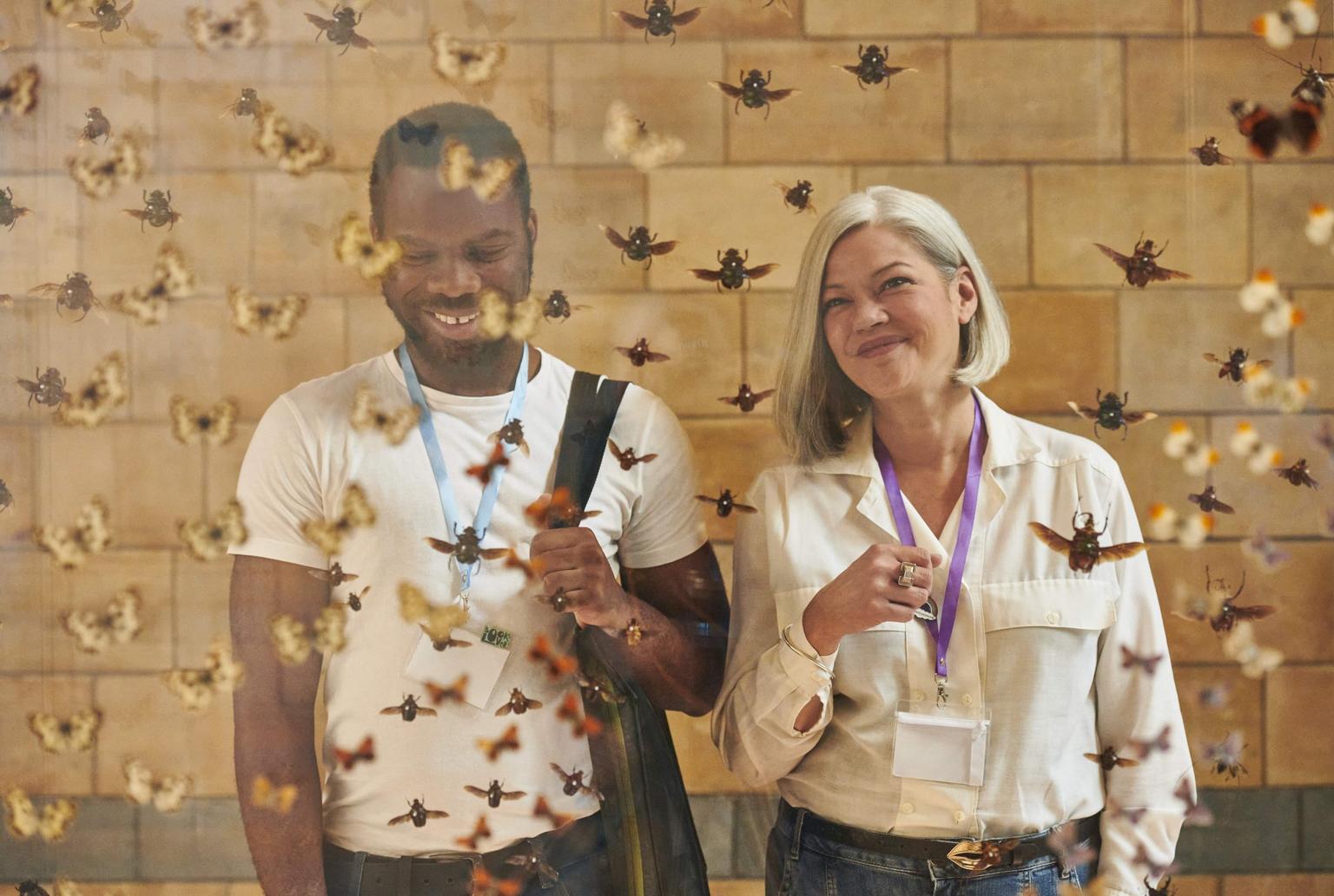 Two smiling museum visitors stand in front of a display of hanging insects.