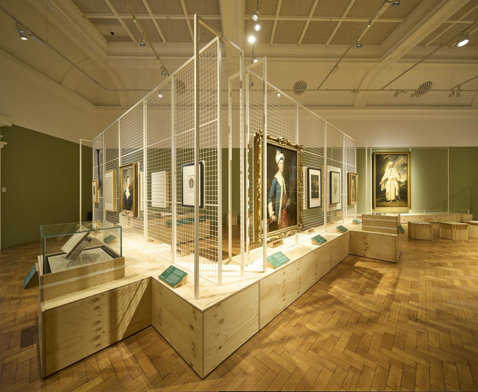 Gallery with portraits displayed on white metal partitions against green walls and a parquet floor.