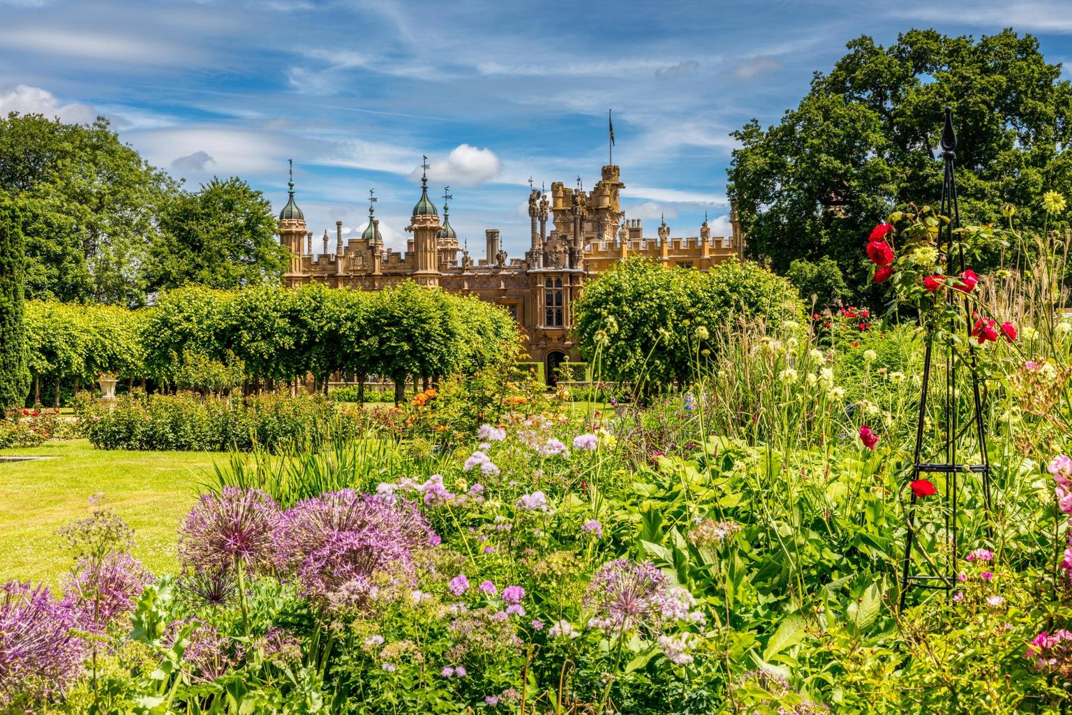 Flourishing gardens with mature plants and trees, an ornate country house in the background