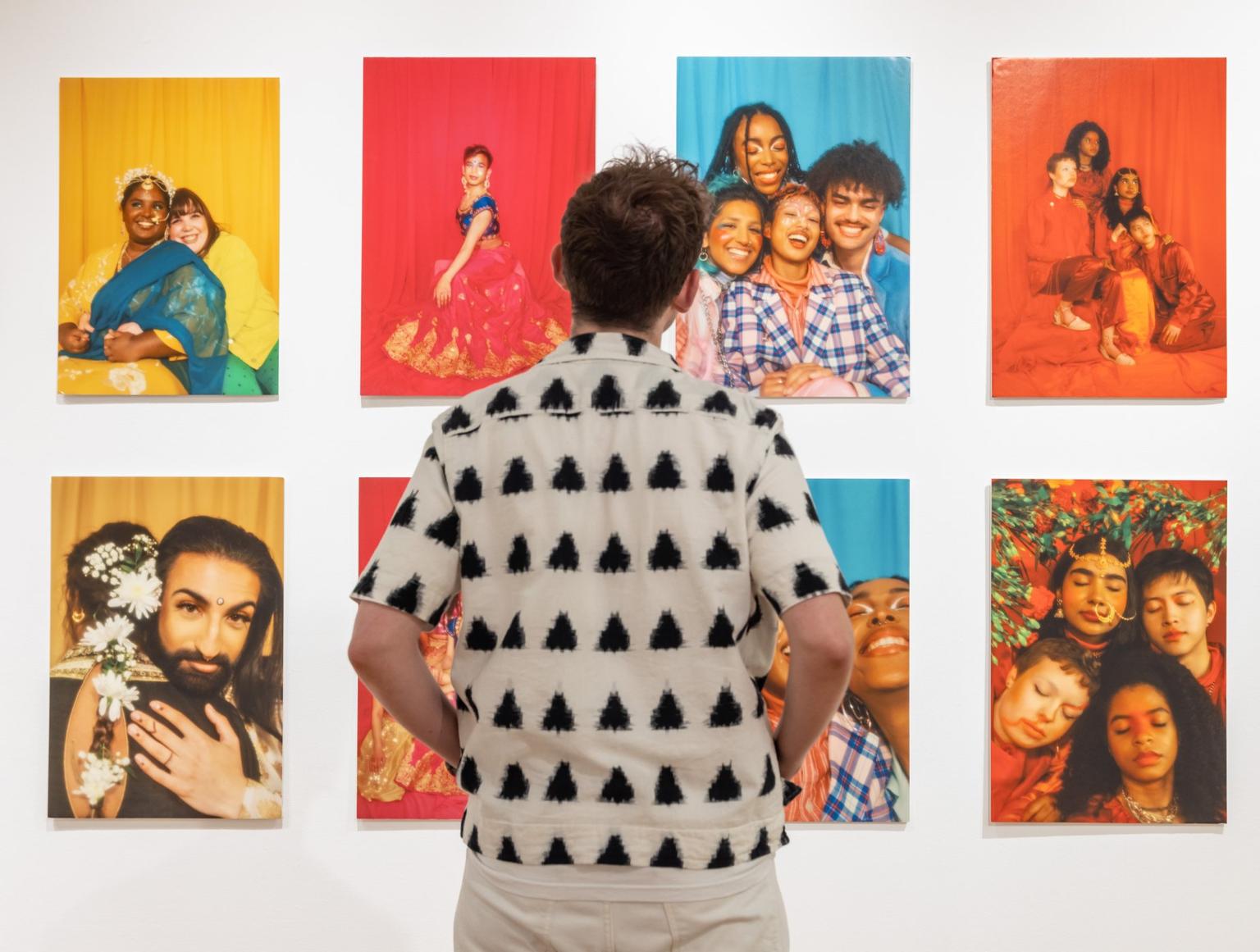 The back of a man standing in front of eight colourful photographs of families and friends