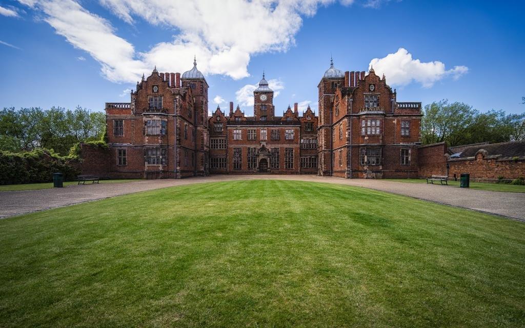 An historic house fronted by a circular lawn with blue skies above